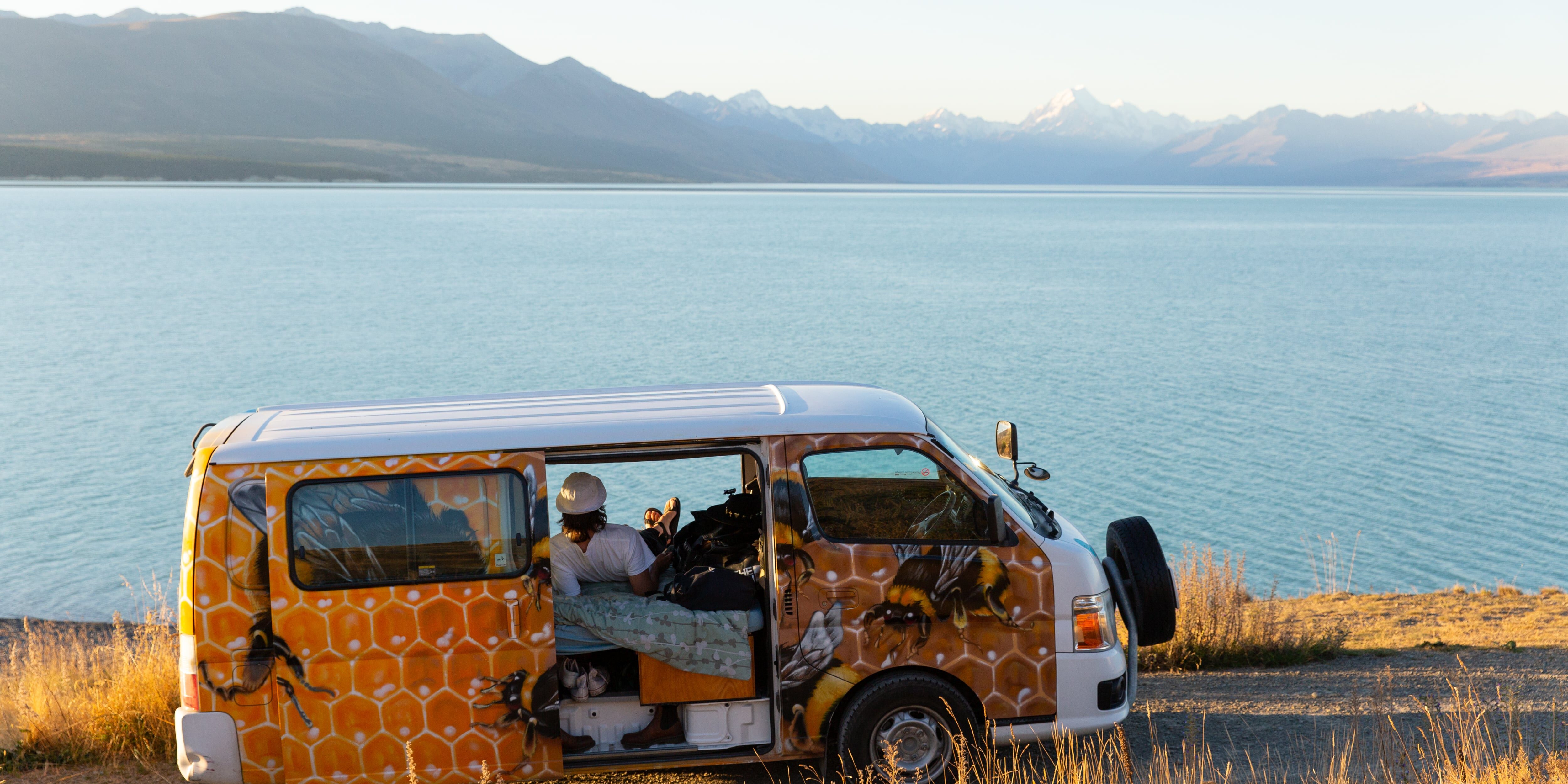 EHG Escape NZ 202003 7759 (1) Person sitting in campervan with lake scenery