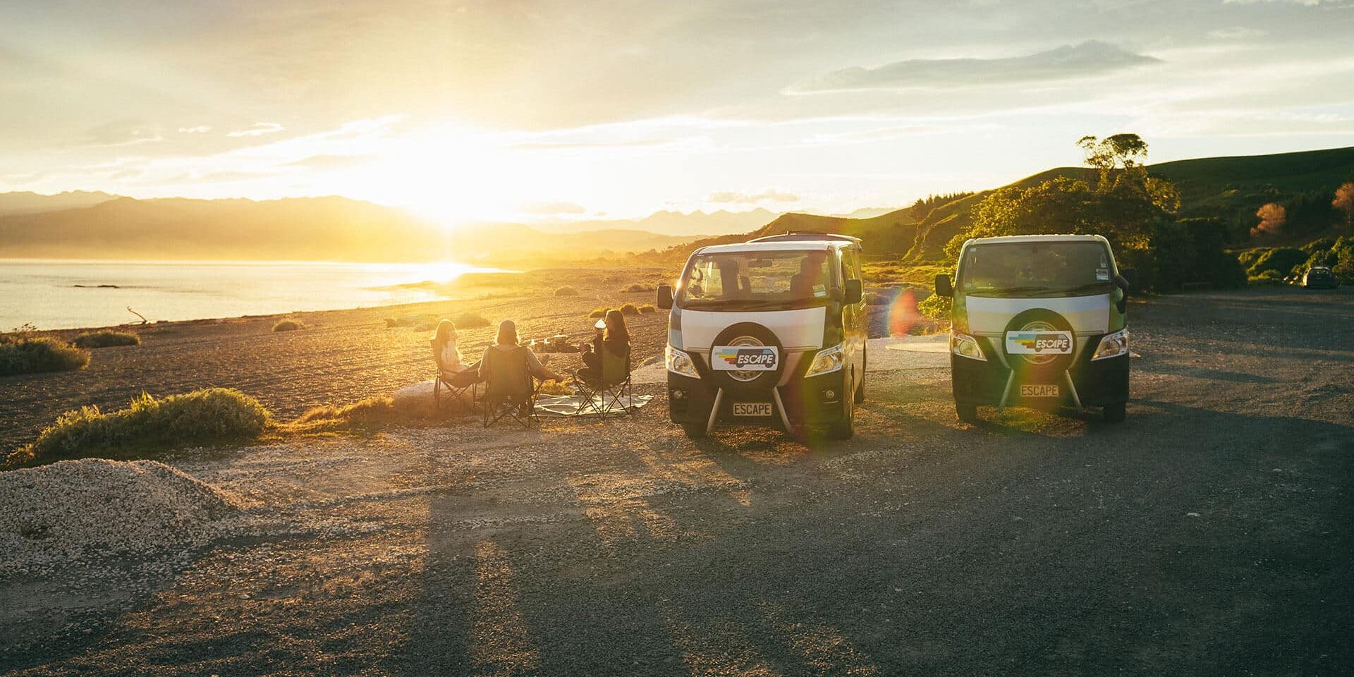 Escape Rentals NZ Compare Our Campervans Tourists enjoy a coffee at sunrise next to their campervans